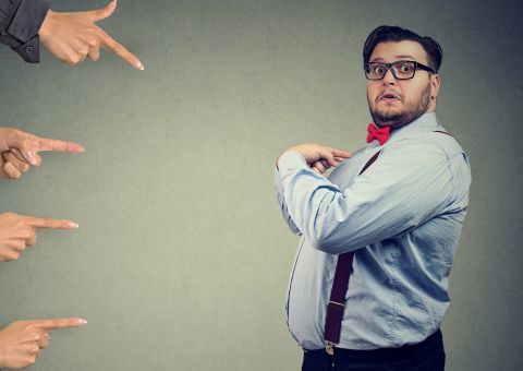 Mehrere Hände zeigen anklagend auf einen überraschten, verdutzten Mann mit Brille.