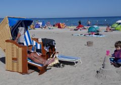 Mann im Strandkorb auf Rügen an der Ostsee mit einem Kind das eine Sandburg baut. KI generiert.