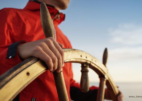 Mann steht am Steuerrad eines Segelboots
