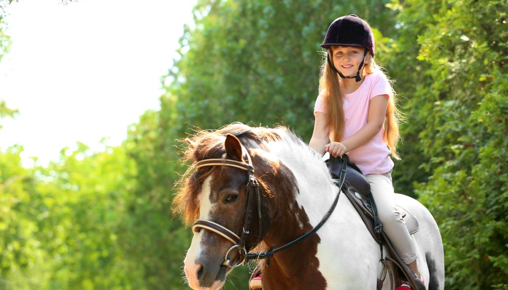 Kleines Mädchen reitet auf einem Pony in einem grünen Park
