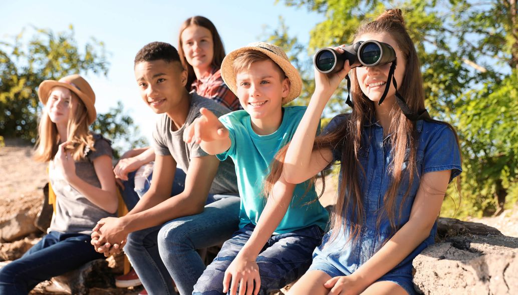Eine Gruppe von Teens sitzt bei Sonnenschein auf Felsen und schaut erfreut in die Ferne