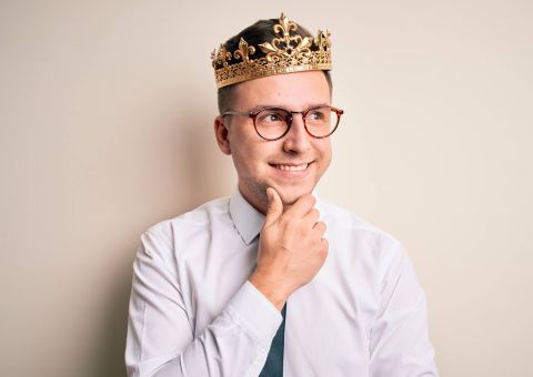 Lächelnder Mann mit Krone und Brille im Hemd denkt nach vor hellem Hintergrund .