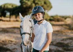Porträt eines Teen mit Helm, das neben seinem weißen Pony steht.