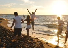 Eine Gruppe fröhlicher junger Leute hat Spaß beim Laufen und Springen am Strand bei Sonnenuntergang.