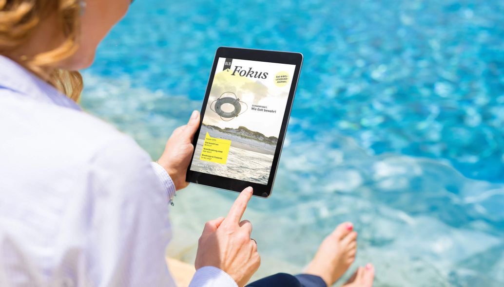 Frau mit weißer Bluse sitzt mit einem I-Pad am Pool und liest das digitale Bibellesebund-Magazin Fokus 3-2024 "Wie Gott bewahrt"