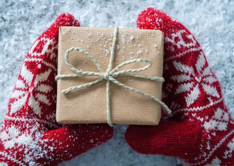Rote Handschuhe halten ein schlicht verpacktes Geschenk im Schnee.