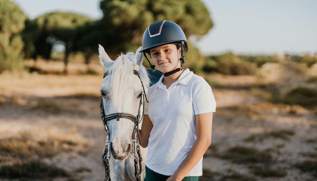 Porträt eines Teen mit Helm, das neben seinem weißen Pony steht.