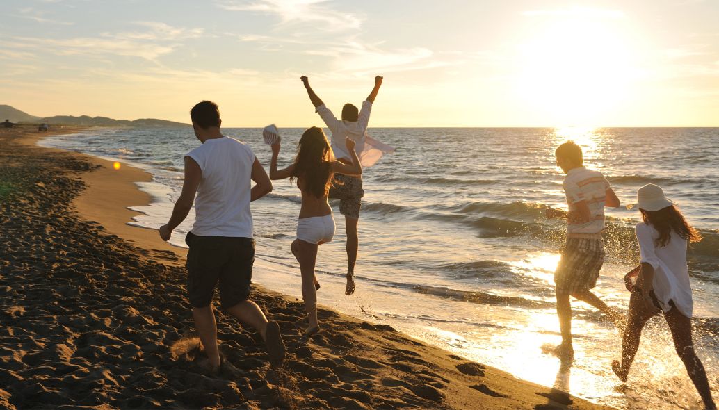 Eine Gruppe fröhlicher junger Leute hat Spaß beim Laufen und Springen am Strand bei Sonnenuntergang.